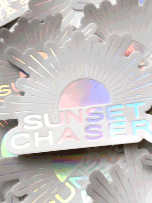 Do you love to chase sunsets? Is sunset your favorite color? Then this Sunset Chaser holographic sticker has your name on it! Printed with a holographic sheen, you'll be mesmerized by how this sticker changes colors as it catches and reflects light -- just like breathtaking sunset! From shades of ocean turquoise to pink sunset, this Sunset Chaser sticker is your little slice of sunset magic. By Samba to the Sea at The Sunset Shop.