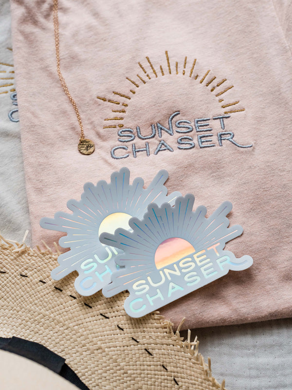 Do you love to chase sunsets? Is sunset your favorite color? Then this Sunset Chaser holographic sticker has your name on it!  Printed with a holographic sheen, you'll be mesmerized by how this sticker changes colors as it catches and reflects light -- just like breathtaking sunset! From shades of ocean turquoise to pink sunset, this Sunset Chaser sticker is your little slice of sunset magic. By Samba to the Sea at The Sunset Shop.