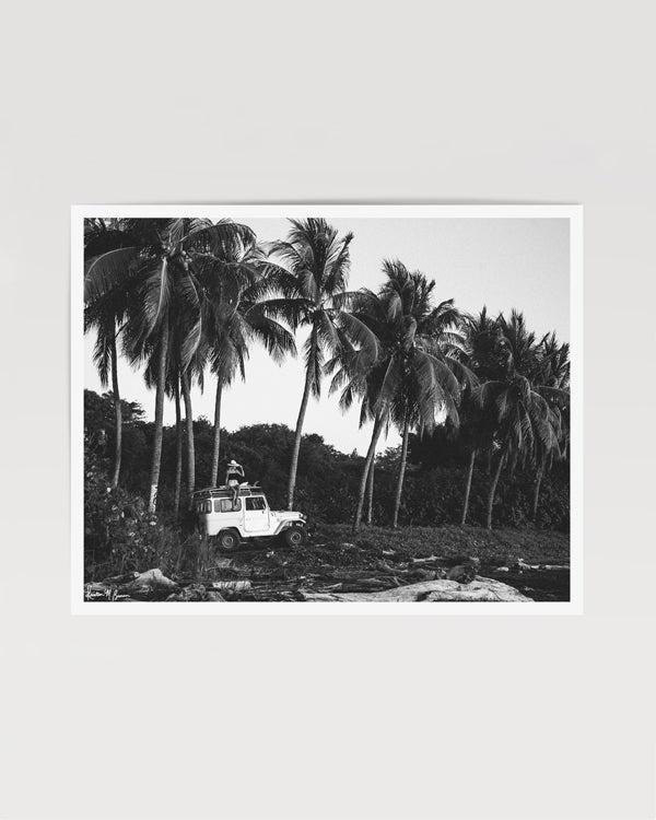  "Surf Bandida" black and white photo print of surfer girl checking the surf with her vintage Toyota FJ40 Land Cruiser racked up with surfboards among the palm trees in Costa Rica. Photographed by Costa Rica photographer Kristen M. Brown of Samba to the Sea for The Sunset Shop.