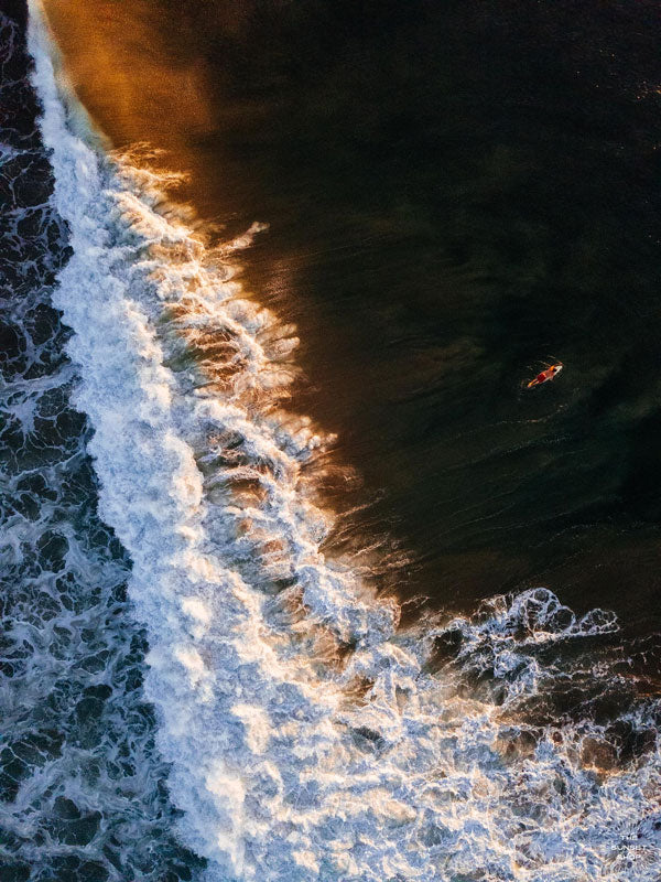 Aerial surfer print by Samba to the Sea at The Sunset Shop. Image is an aerial photo of surfer paddling out to surf in Tamarindo, Costa Rica during golden hour.