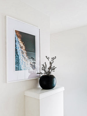 Framed aerial surfer print "The Rush" from The Sunset Shop by Ash Interiors. Aerial surfer print by Samba to the Sea at The Sunset Shop. Image is an aerial photo of surfer paddling out to surf in Tamarindo, Costa Rica during golden hour.
