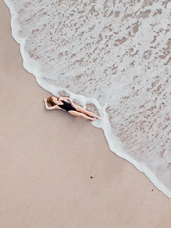 Woman laying on the beach as the waves reach her feet in Costa Rica. Photographed by Samba to the Sea for The Sunset Shop. 