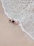 Woman laying on the beach as the waves reach her feet in Costa Rica. Photographed by Samba to the Sea for The Sunset Shop. 