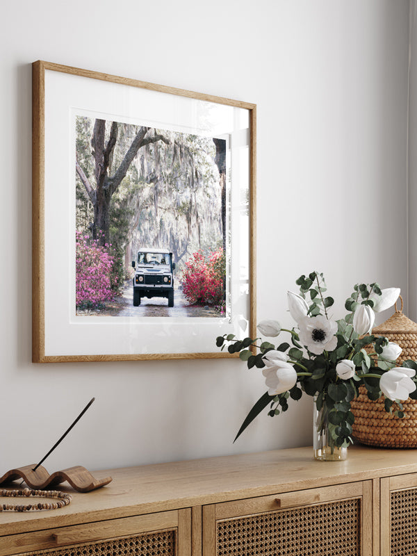 Land Rover photo print wall art hanging above beautiful cane console. You just know that an adventure is calling when it&#39;s that time of year with Savannah&#39;s azaleas are vibrantly blooming. So hop on in to this dreamy white Land Rover Defender and experience the magic that is Savannah in full bloom. &quot; &#39;Venture Rover&quot; Land Rover photo print by Kristen M. Brown of Samba to the Sea for The Sunset Shop.