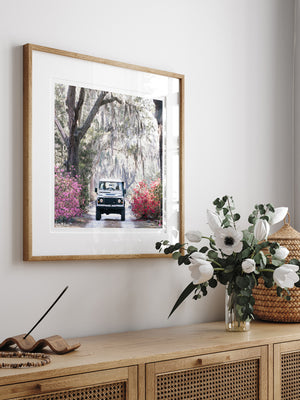 Land Rover photo print wall art hanging above beautiful cane console. You just know that an adventure is calling when it's that time of year with Savannah's azaleas are vibrantly blooming. So hop on in to this dreamy white Land Rover Defender and experience the magic that is Savannah in full bloom. " 'Venture Rover" Land Rover photo print by Kristen M. Brown of Samba to the Sea for The Sunset Shop.
